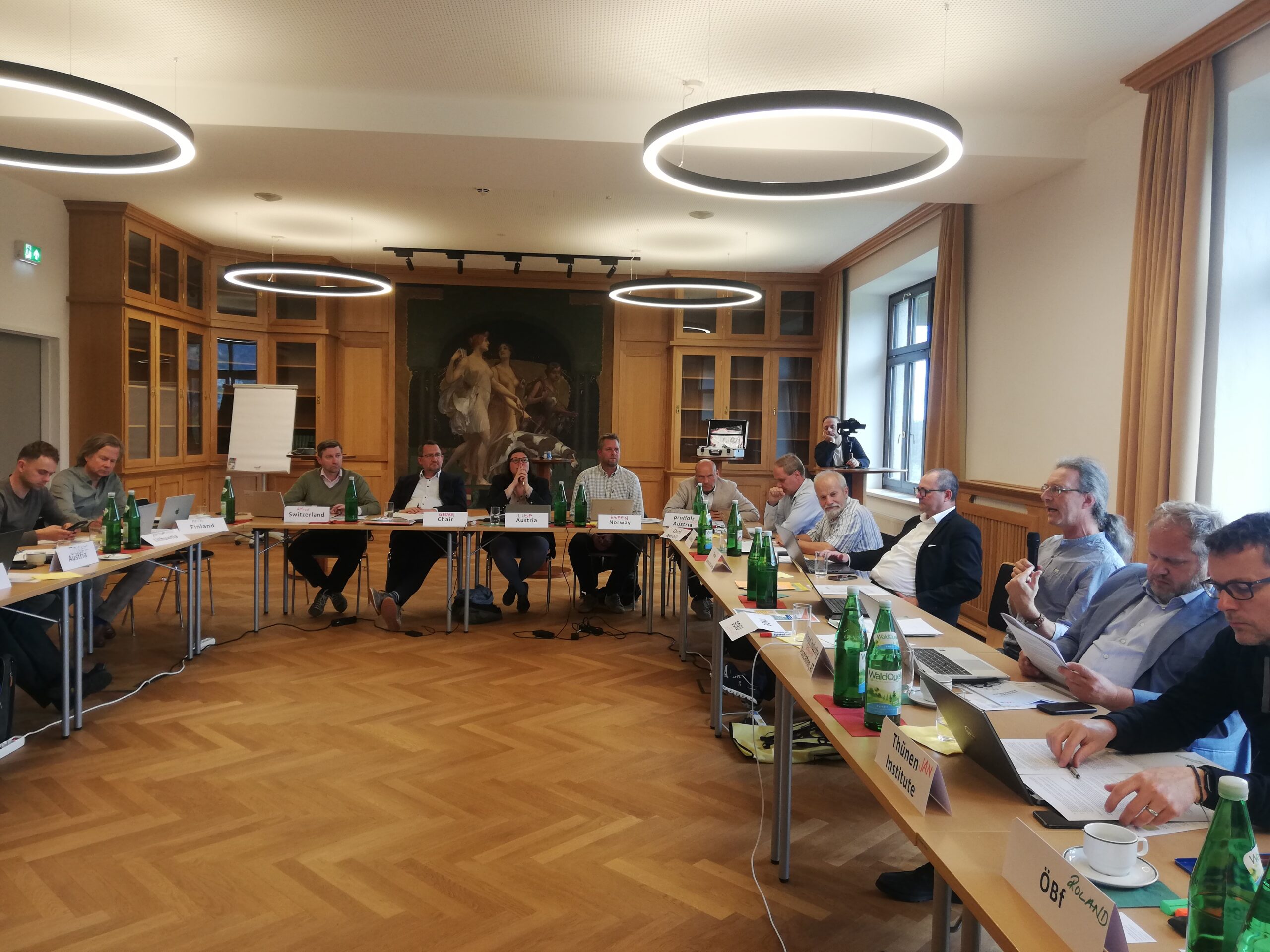 12 men and a woman with white nameplates in front of them, sitting in for a meeting