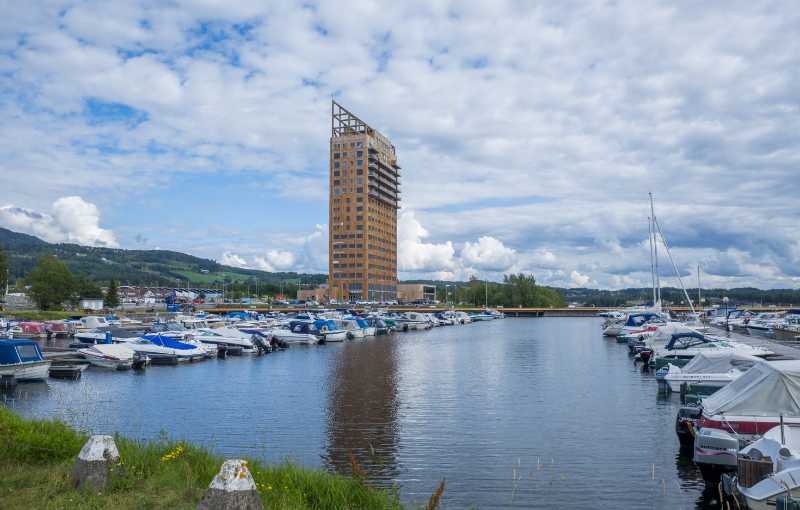 A tall timber skyscraper overlooking a body of water that is filled with boats.